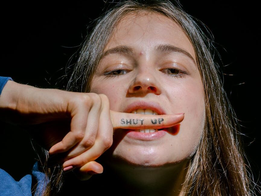 a young woman with shut up note on index finger